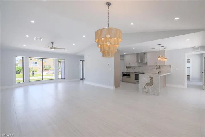 Unfurnished living room featuring light tile patterned floors, ceiling fan with notable chandelier, sink, and lofted ceiling