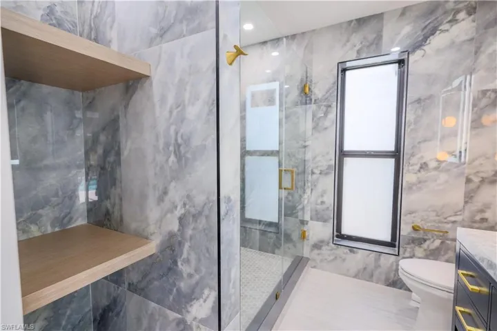 Bathroom featuring a shower with shower door, toilet, tile patterned floors, and tile walls