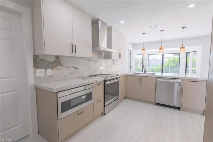 Kitchen featuring light brown cabinets, wall chimney exhaust hood, tasteful backsplash, appliances with stainless steel finishes, and sink