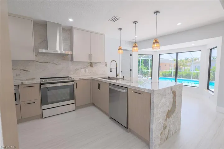 Kitchen featuring sink, appliances with stainless steel finishes, light stone counters, light tile patterned floors, and wall chimney range hood
