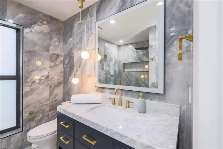 Bathroom with toilet, walk in shower, vanity, and tile walls