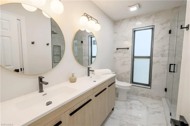 Bathroom featuring tile patterned flooring, toilet, double vanity, and a shower with door