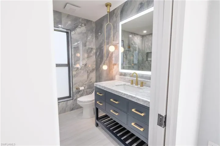 Bathroom featuring toilet, tile patterned flooring, vanity, tile walls, and walk in shower