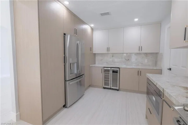 Kitchen with light tile patterned floors, backsplash, stainless steel fridge, and beverage cooler