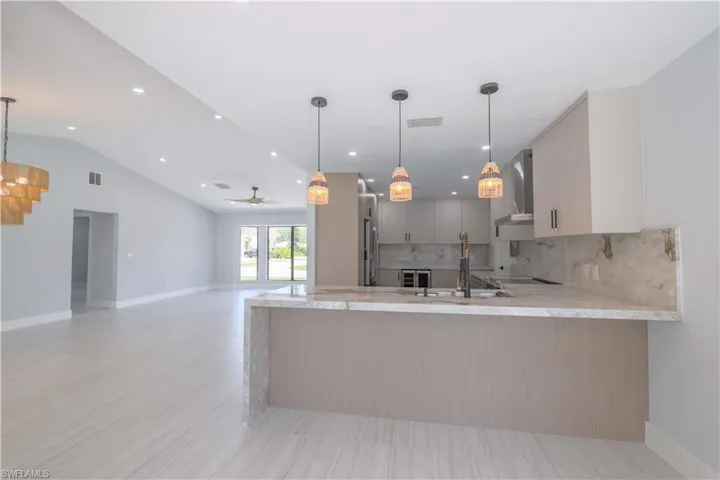 Kitchen featuring wall chimney range hood, decorative backsplash, ceiling fan, sink, and light tile patterned flooring