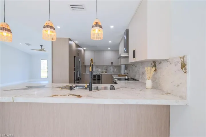 Kitchen featuring decorative light fixtures, light stone countertops, stainless steel refrigerator with ice dispenser, tasteful backsplash, and white cabinets
