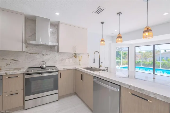 Kitchen with sink, tasteful backsplash, stainless steel appliances, pendant lighting, and wall chimney range hood