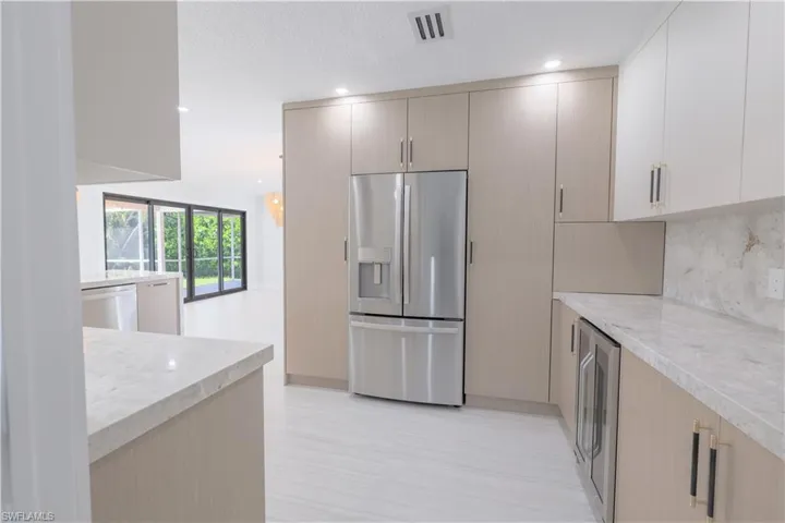 Kitchen with light brown cabinets, stainless steel refrigerator with ice dispenser, tasteful backsplash, light stone counters, and dishwasher