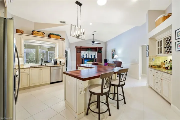 Kitchen featuring backsplash, a breakfast bar, stainless steel appliances, vaulted ceiling, and light tile patterned floors