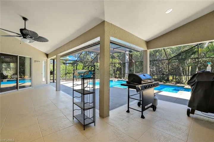 Swimming pool with a sunroom, a patio area, glass enclosure, and a grill