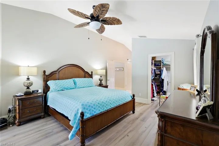 Bedroom with vaulted ceiling, light wood-style floors, a walk in closet, and a ceiling fan