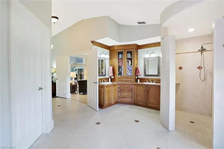 Full bath featuring double vanity, vaulted ceiling, walk in shower, and light tile patterned floors