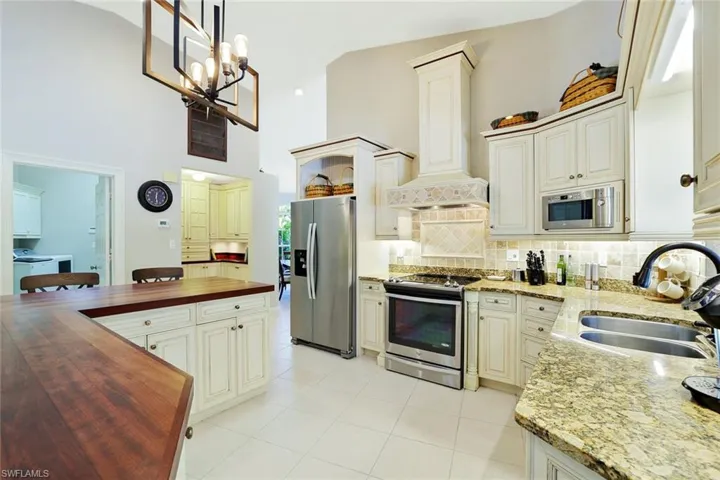 Kitchen featuring tasteful backsplash, appliances with stainless steel finishes, wood counters, premium range hood, and light tile patterned floors