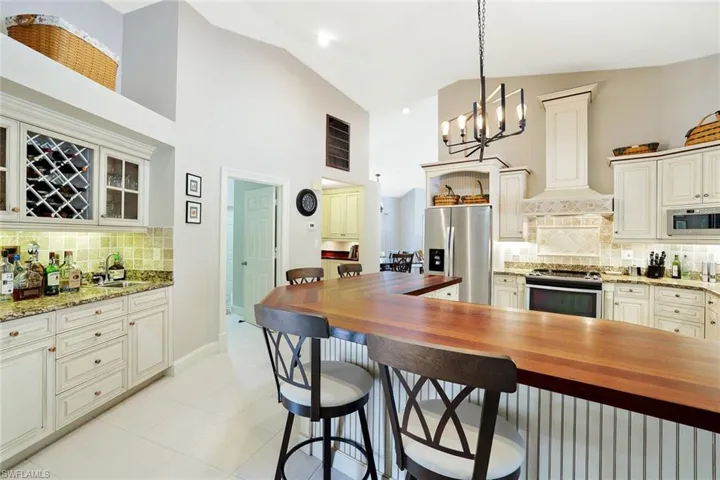Kitchen featuring decorative backsplash, dark stone counters, appliances with stainless steel finishes, a kitchen bar, and high vaulted ceiling
