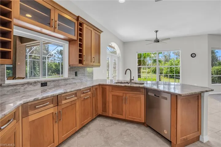 Kitchen with ceiling fan, kitchen peninsula, backsplash, light tile flooring, and dishwasher