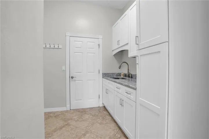 Kitchen featuring white cabinets, sink, light stone countertops, and light tile floors