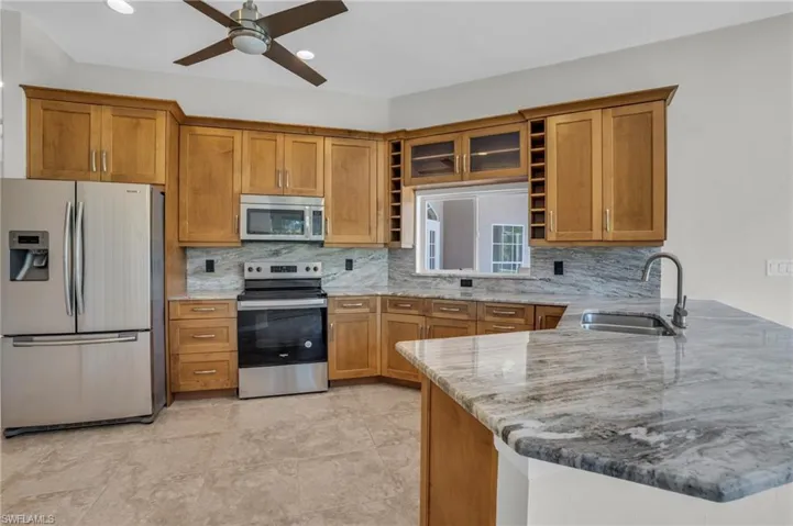 Kitchen featuring kitchen peninsula, stainless steel appliances, ceiling fan, tasteful backsplash, and sink