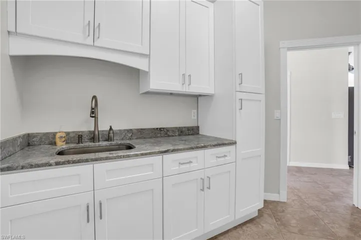Kitchen featuring stone countertops, sink, white cabinetry, and light tile floors