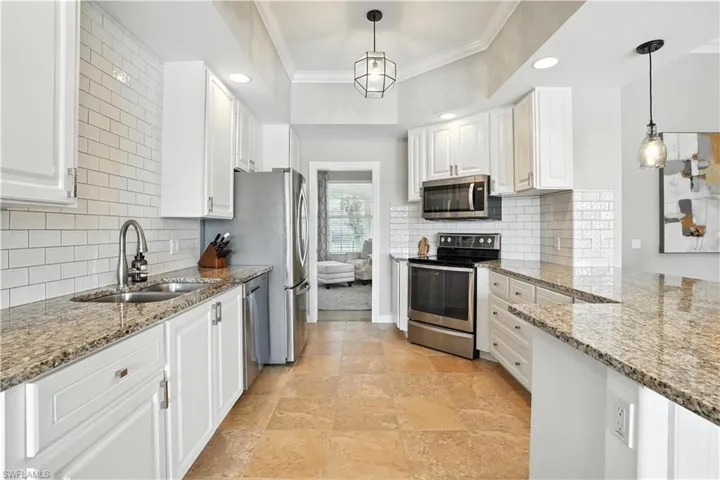 Kitchen with appliances with stainless steel finishes, white cabinets, crown molding, light stone countertops, and recessed lighting