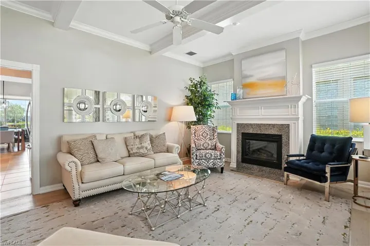 Living area with beamed ceiling, wood finished floors, crown molding, a high end fireplace, and ceiling fan