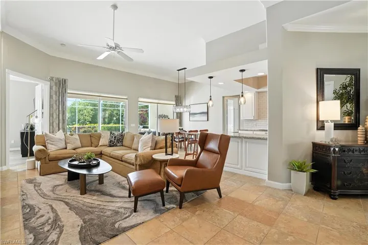 Living room featuring crown molding, ceiling fan, and stone tile flooring