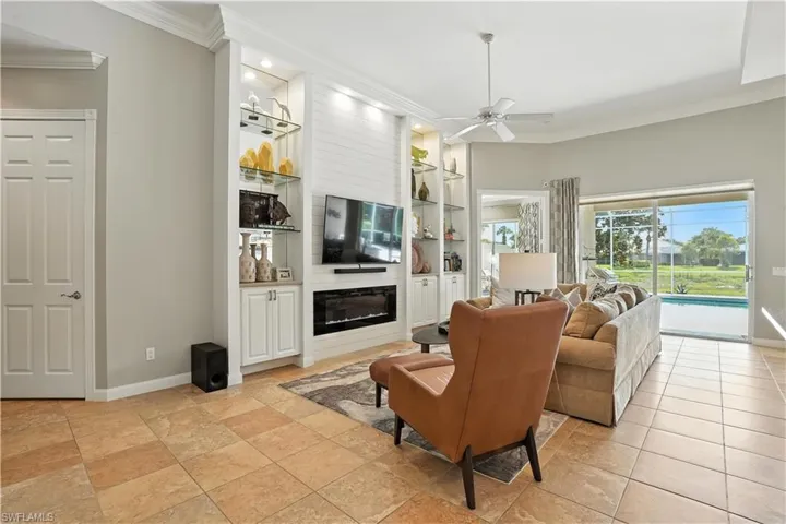 Living area with crown molding, built in shelves, ceiling fan, and a fireplace