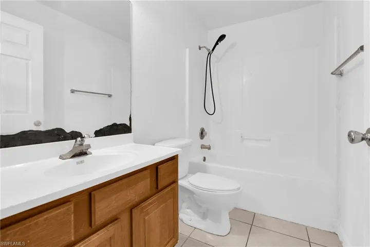 Bathroom featuring a wood-finish vanity with a white countertop and integrated sink, a large wall-mounted mirror, a white toilet, and a white tub/shower combination with a handheld showerhead