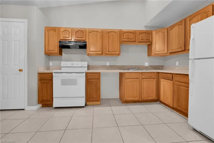 Kitchen featuring wood cabinetry, light-toned countertops, white appliances, and tiled flooring