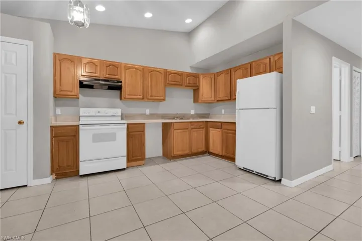 Kitchen featuring wood-finish cabinetry, light-toned countertops, white appliances, and square tile flooring