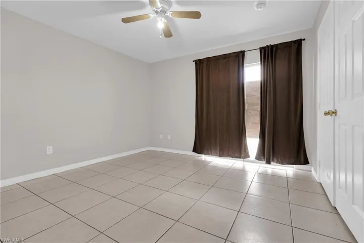Room featuring neutral wall paint, tiled flooring, a ceiling fan with light fixture, and a white paneled door with brass hardware