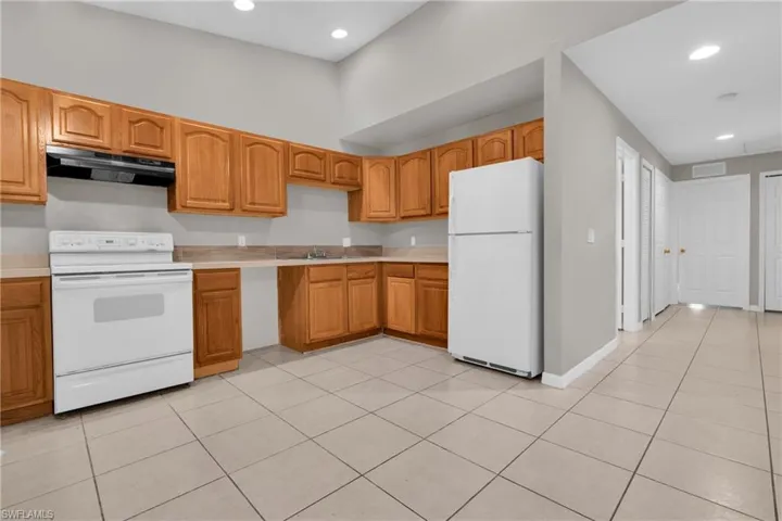 Kitchen featuring extensive wood cabinetry, white appliances, square tile flooring, a built-in sink, and recessed ceiling lighting