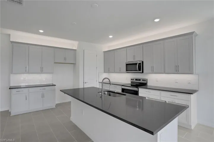 Kitchen with decorative backsplash, stainless steel appliances, a center island with sink, recessed lighting, and dark stone countertops