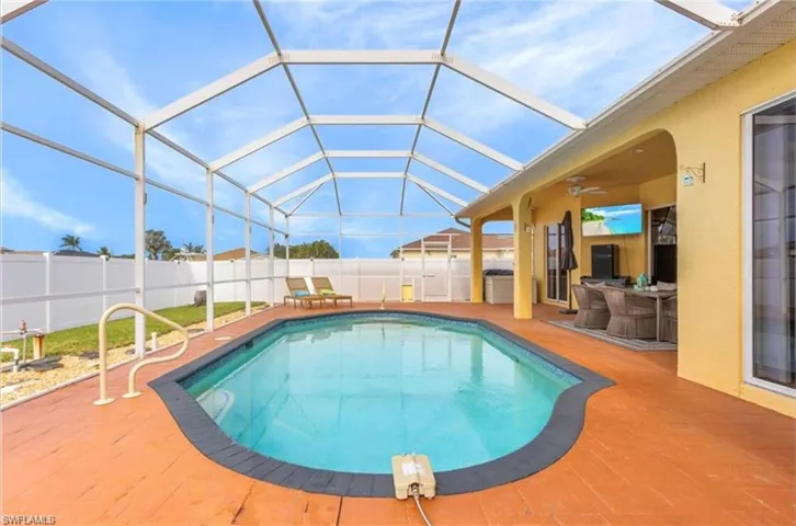 Screened-in outdoor pool featuring a contoured design, a durable hardscape deck, and an adjacent covered patio