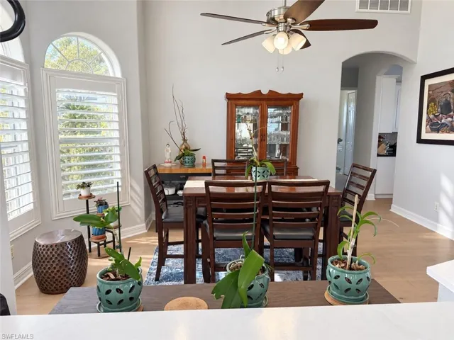 Dining area featuring vaulted ceilings, wood-finish flooring, plantation shutters, an arched window, and a ceiling fan with integrated lighting