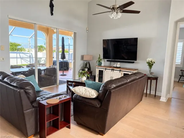 Light wood-finish flooring, vaulted ceiling, ceiling fan with integrated lighting, sliding glass doors, and a built-in entertainment console