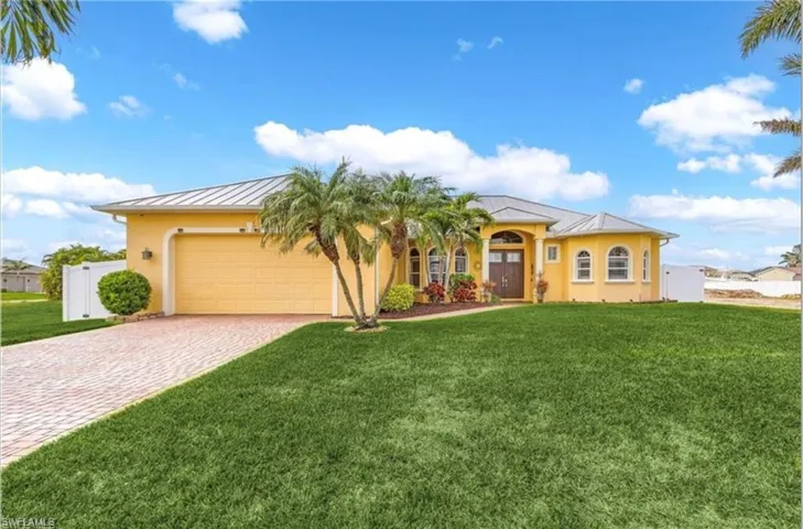 Stucco exterior with arched windows, a metal roof, a paver driveway, and mature landscaping