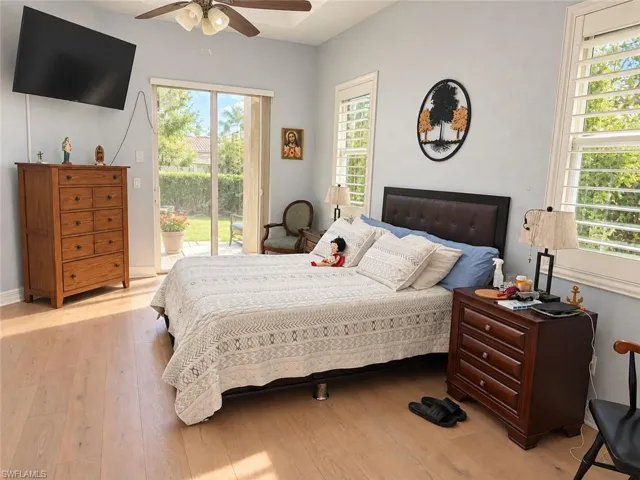 Wood-finish flooring, ceiling fan, sliding glass door, plantation shutters, and a paneled headboard