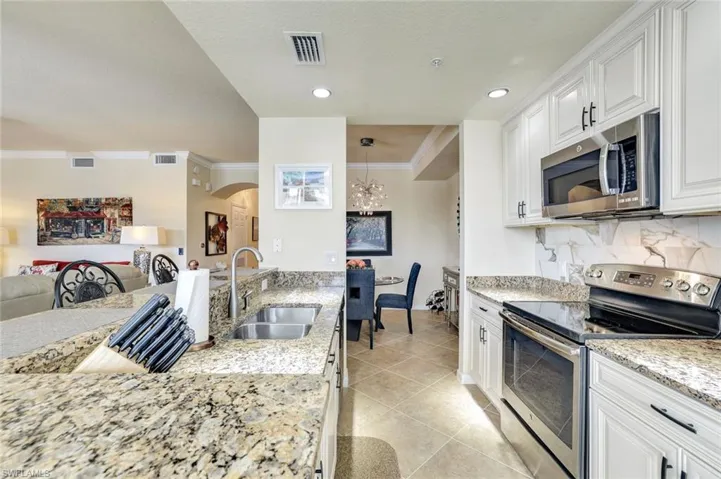 Kitchen featuring appliances with stainless steel finishes, arched walkways, light stone countertops, white cabinets, and light tile patterned floors