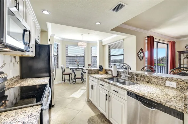 Kitchen with white cabinetry, appliances with stainless steel finishes, light stone counters, decorative light fixtures, and light tile patterned flooring
