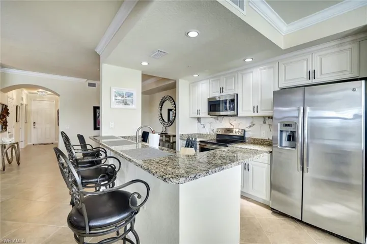 Kitchen with crown molding, stainless steel appliances, a breakfast bar area, arched walkways, and light stone counters