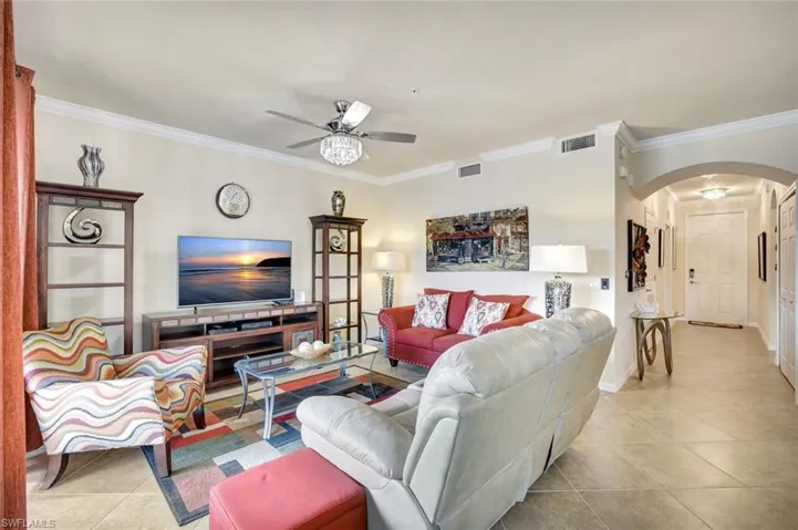 Living room with light tile patterned floors, arched walkways, ornamental molding, and ceiling fan
