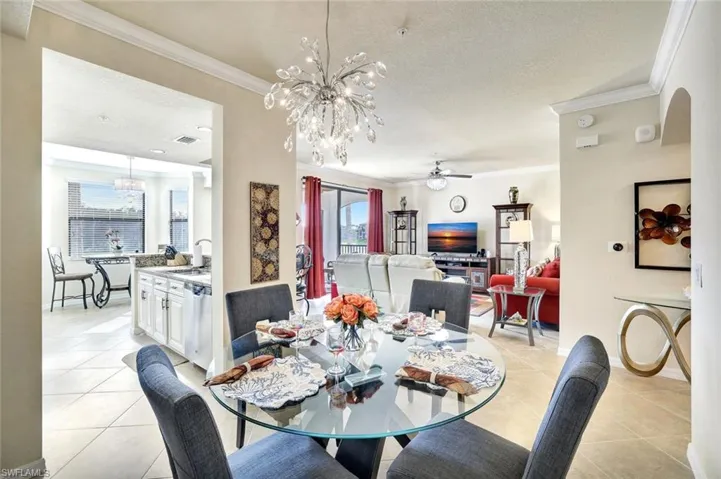 Dining area with a ceiling fan, crown molding, a textured ceiling, a chandelier, and light tile patterned floors
