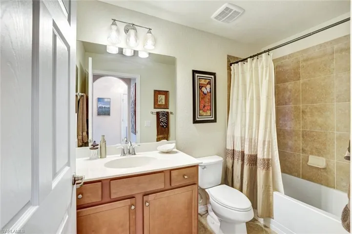Full bathroom featuring shower / bath combination with curtain, vanity, and a textured wall