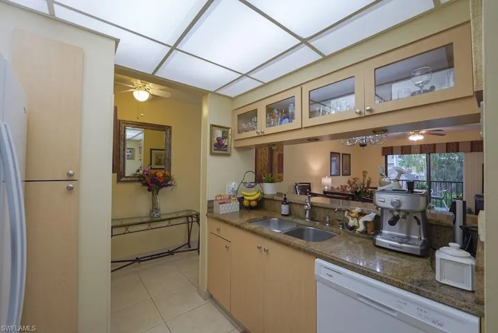 Kitchen featuring dishwasher, ceiling fan, glass insert cabinets, light tile patterned floors, and dark stone countertops