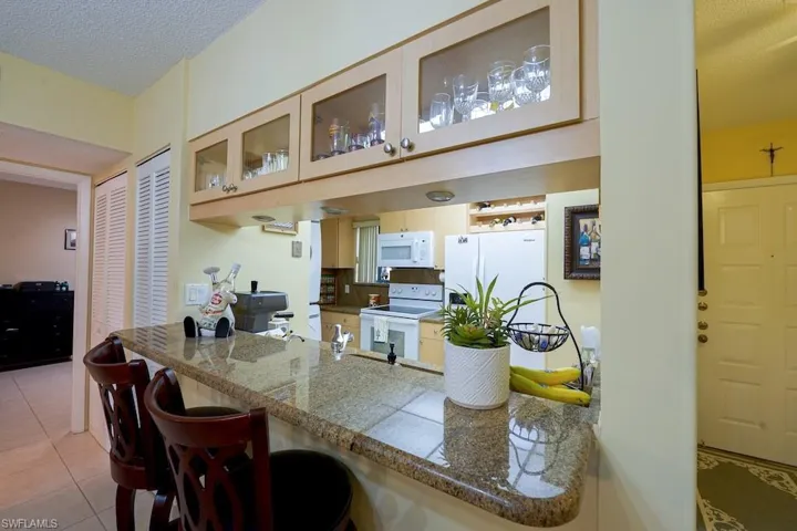 Kitchen featuring white appliances, glass insert cabinets, light tile patterned floors, a textured ceiling, and a peninsula