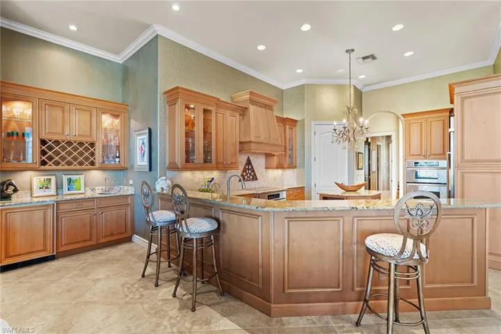 Kitchen with a breakfast bar area, glass insert cabinets, a chandelier, crown molding, and wallpapered walls
