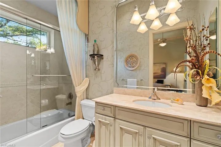 Bathroom with enclosed tub / shower combo, vanity, wallpapered walls, and a ceiling fan