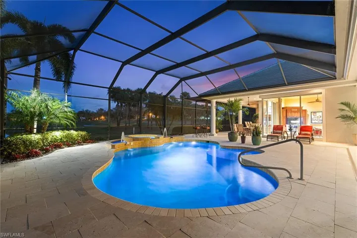 Pool at dusk with a patio, glass enclosure, a sunroom, and a pool with connected hot tub