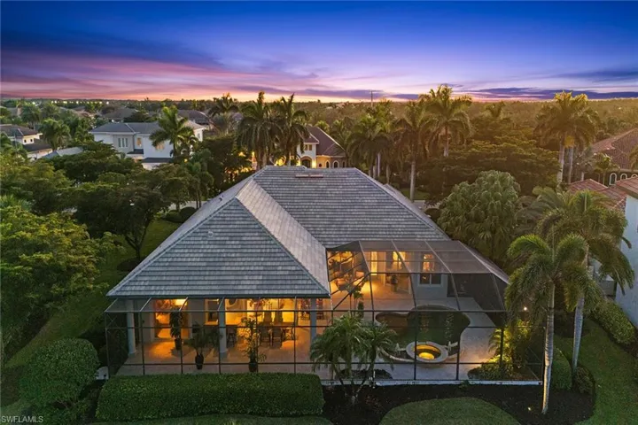 Back of property at dusk featuring glass enclosure, an outdoor pool, and a jacuzzi