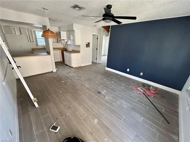 Unfurnished living room featuring ceiling fan, a textured ceiling, and dark hardwood / wood-style floors